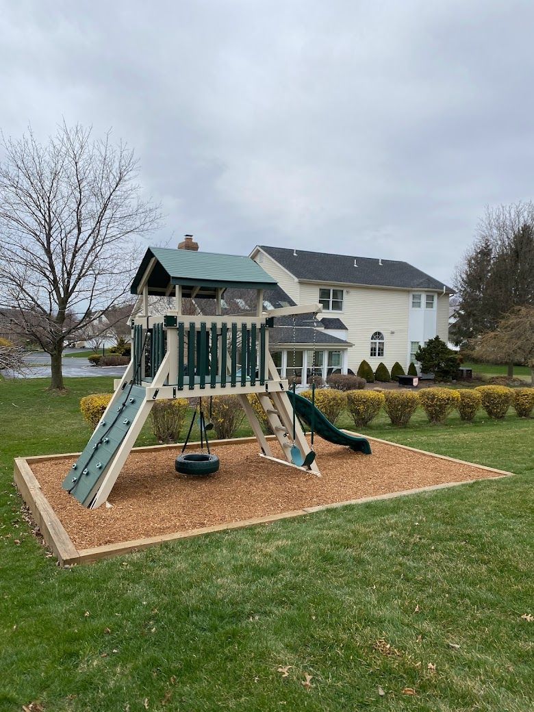 A playground set in the backyard of a house with a slide and swings.