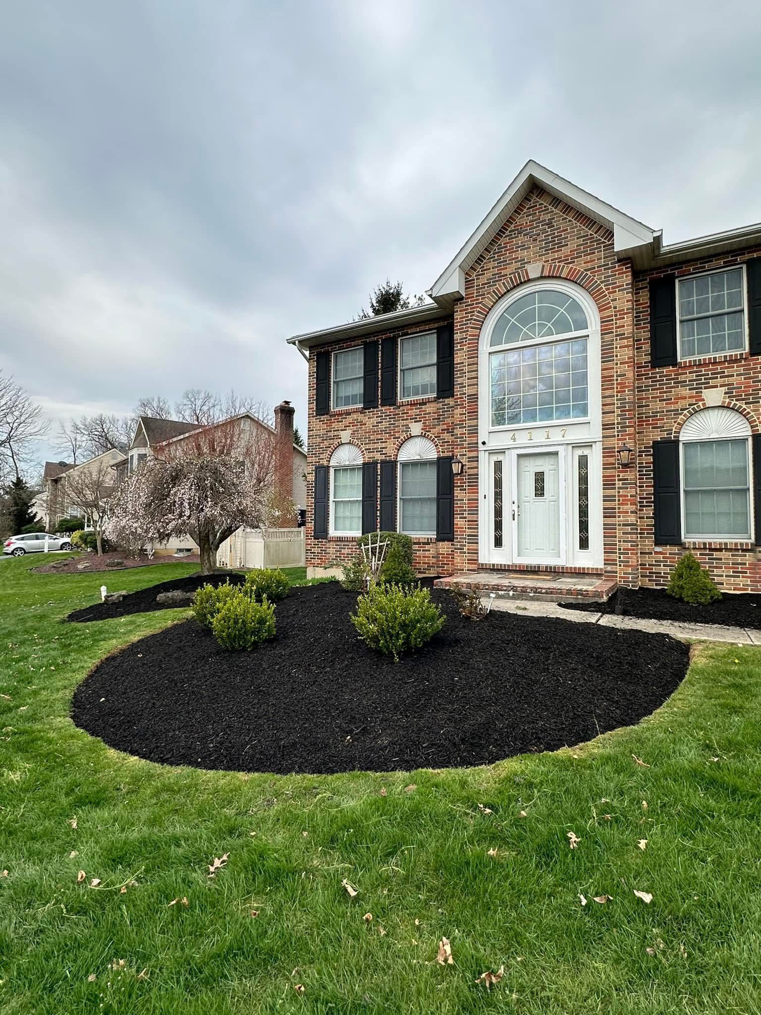 A large brick house with black shutters is sitting on top of a lush green lawn.