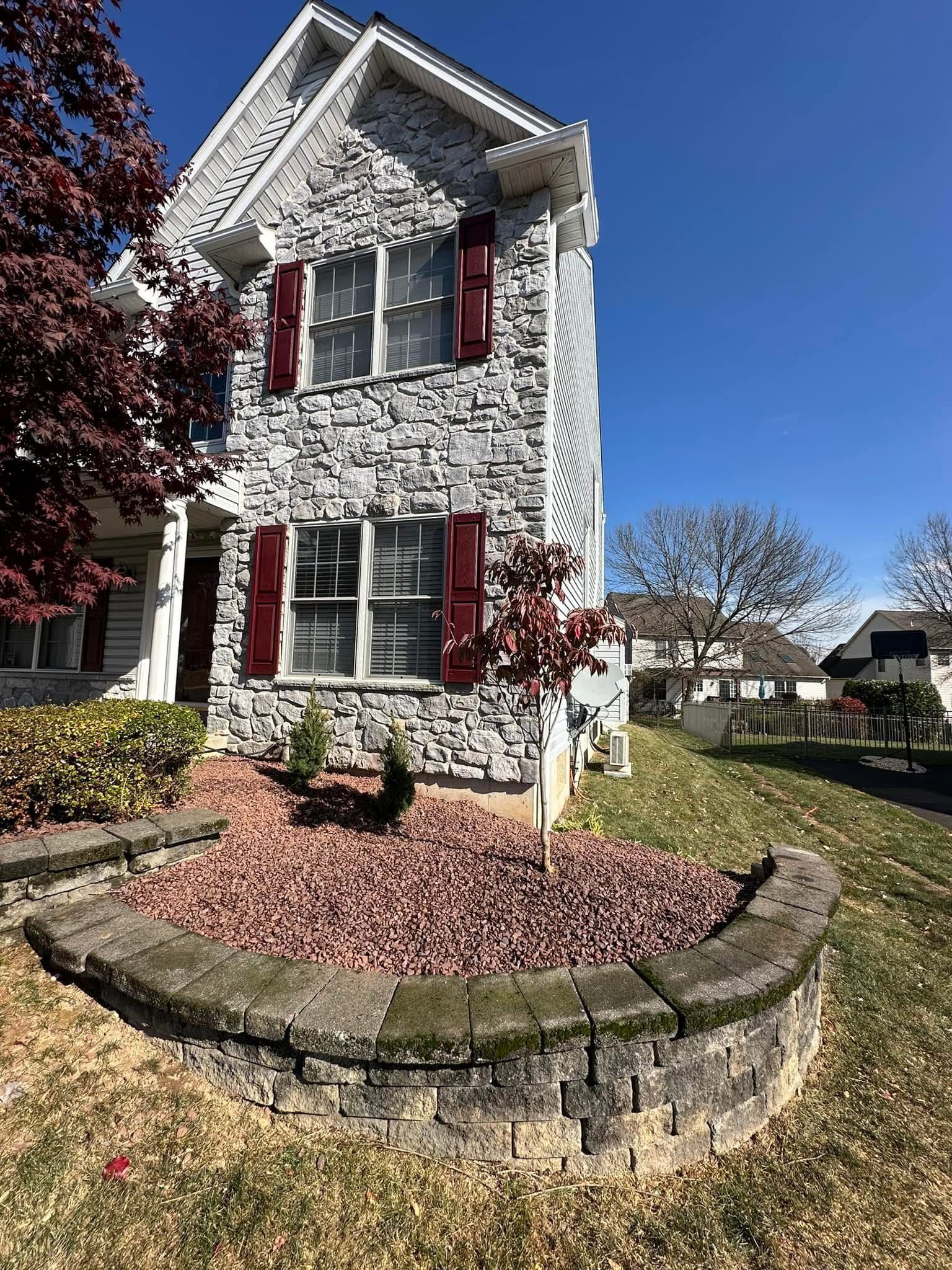 A white house with red shutters and a stone wall in front of it.
