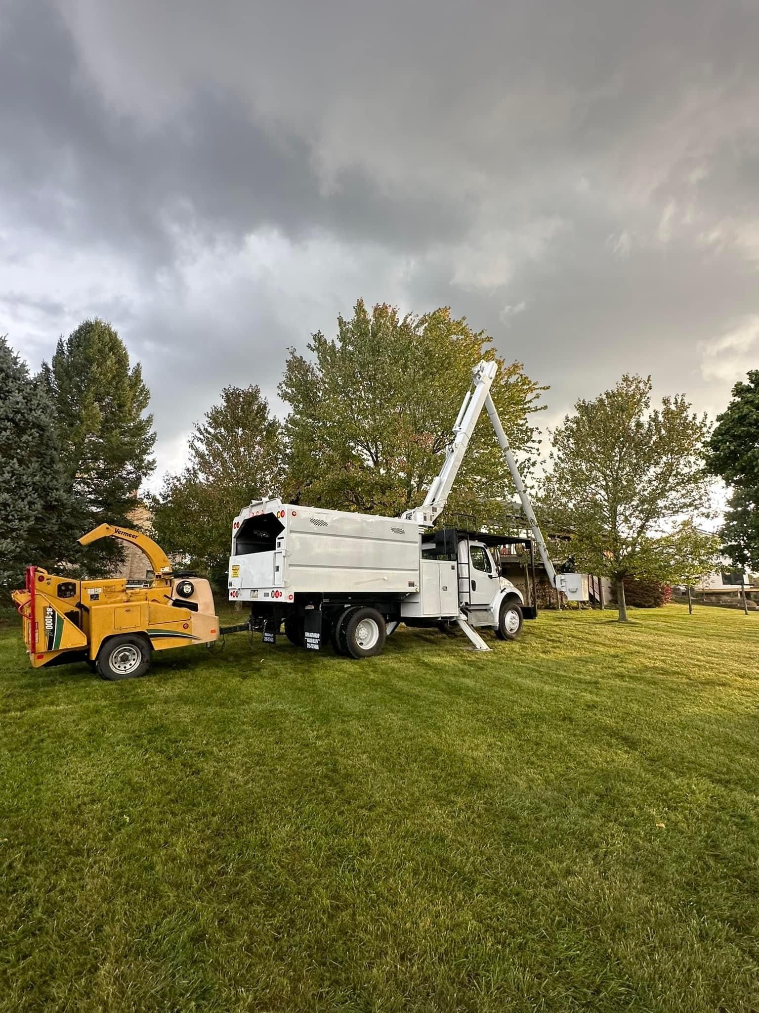 A white truck is parked in a grassy field next to a tree chipper.