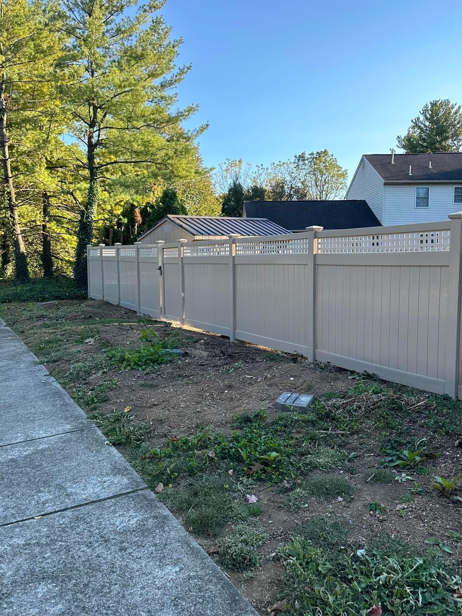 A wooden fence surrounds a yard next to a sidewalk and a house.