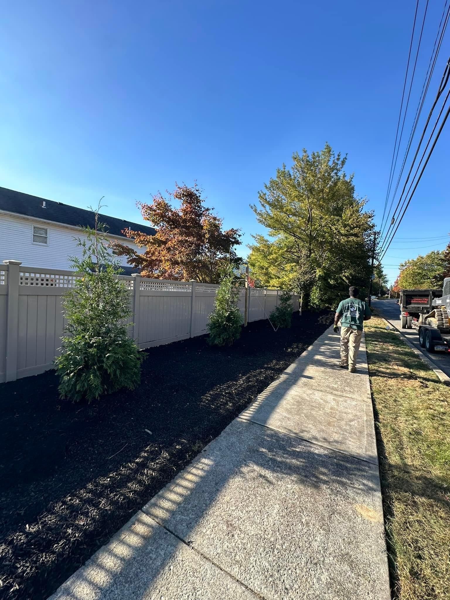 A person is walking down a sidewalk next to a fence.