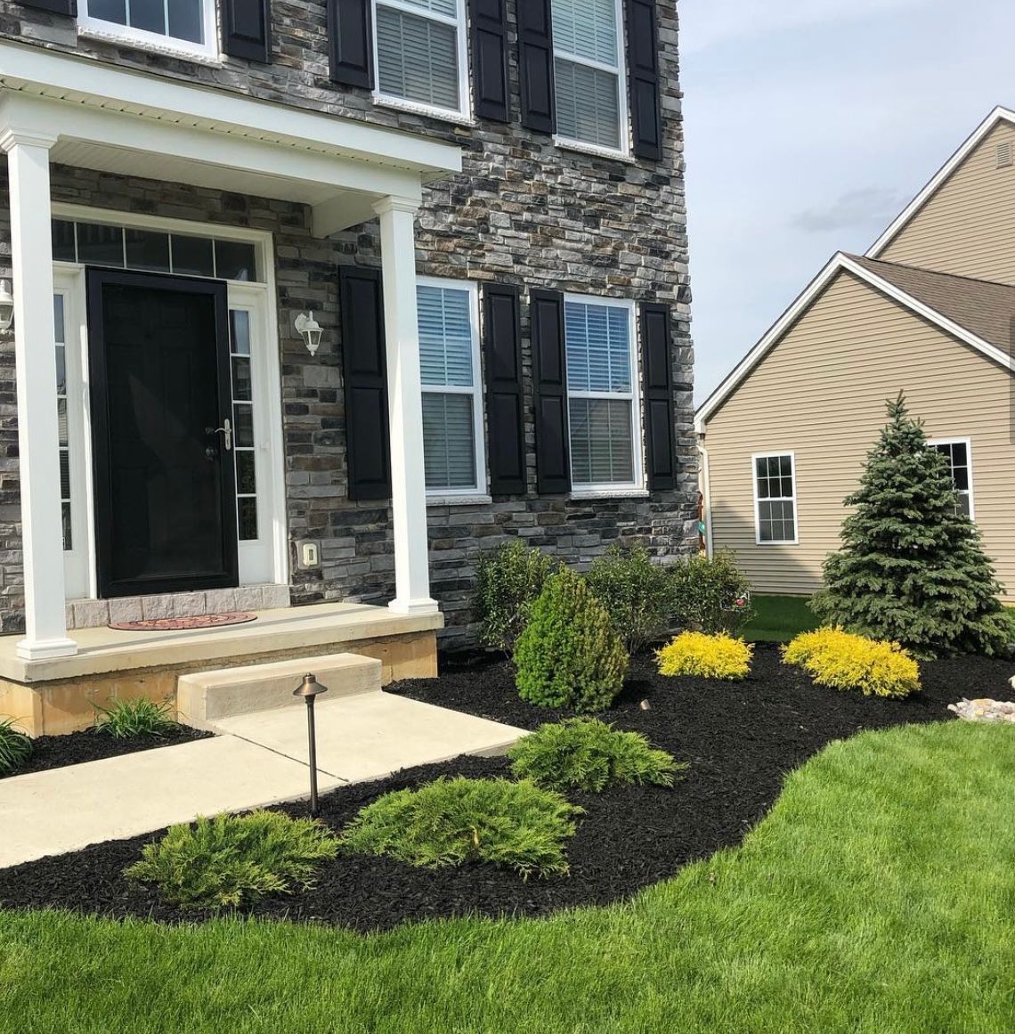 A house with a porch and a lush green lawn in front of it.