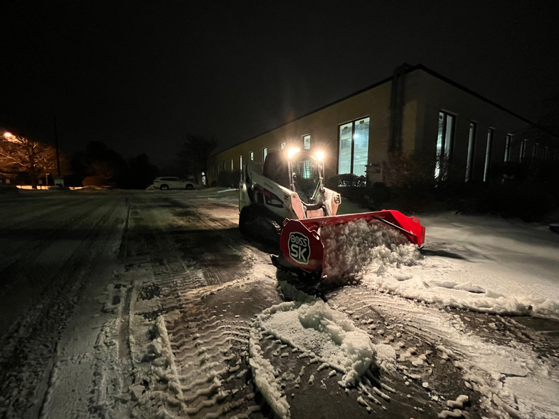 A snow plow is clearing snow from a parking lot at night.