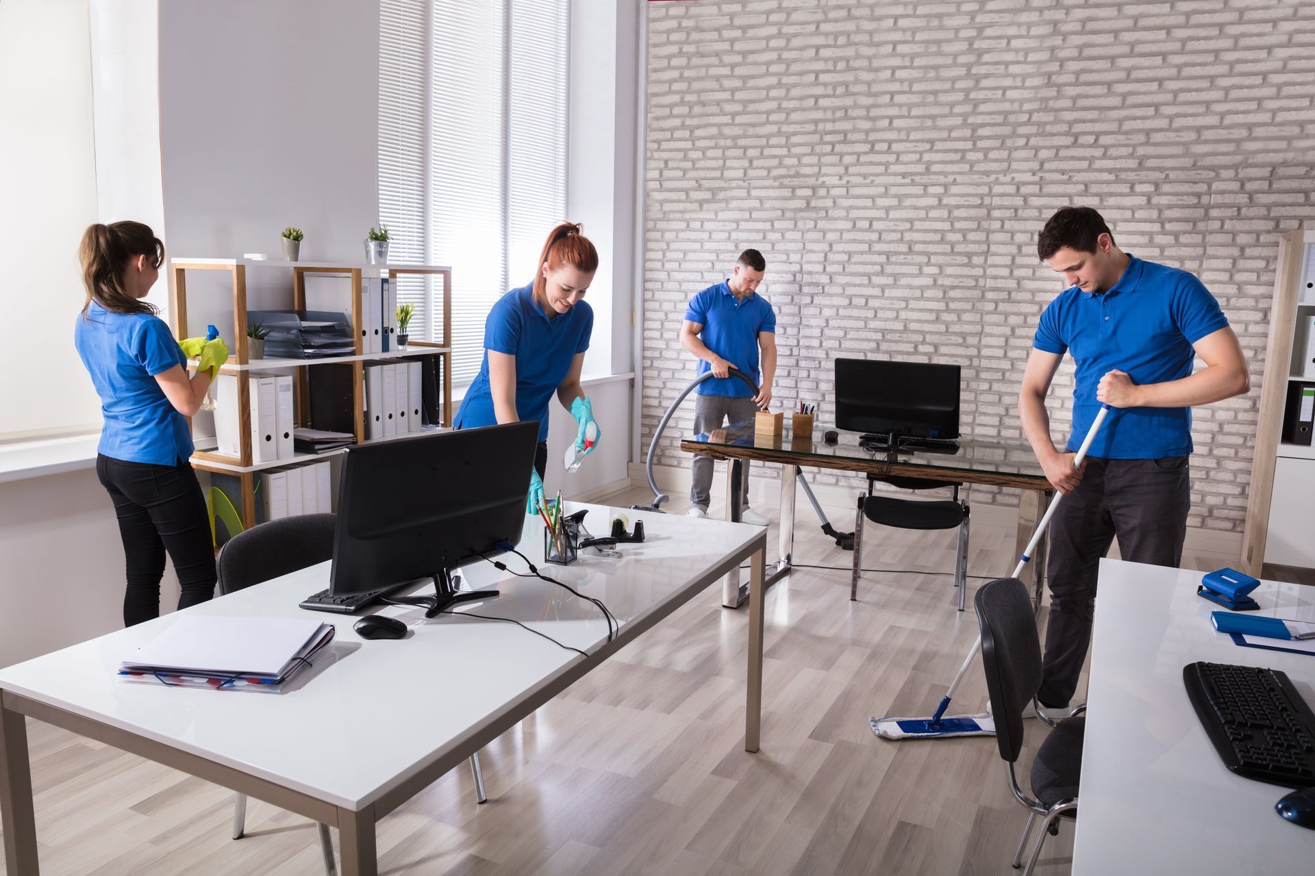Office cleaning crew in blue shirts; four people cleaning desks and floors.
