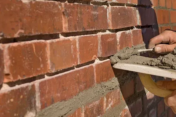 A person is laying bricks on a brick wall with a trowel.