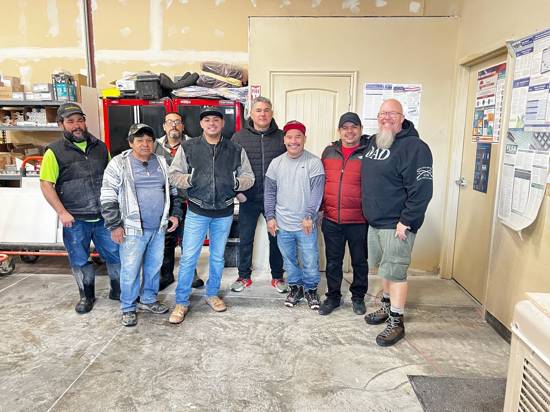 Group of people smiling in a workshop, some wearing work attire
