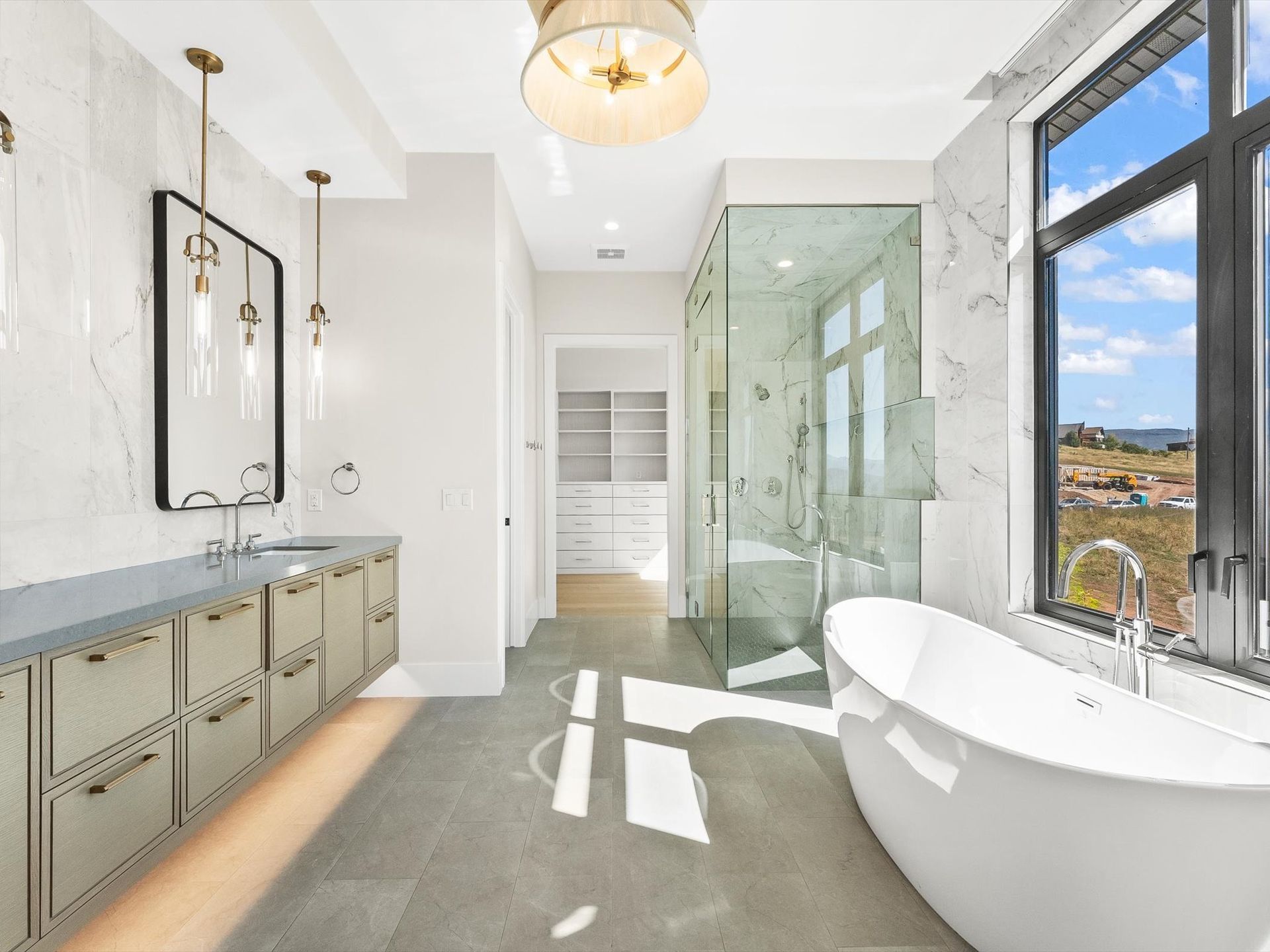 Luxury bathroom with marble walls, freestanding tub, and large window overlooking a view