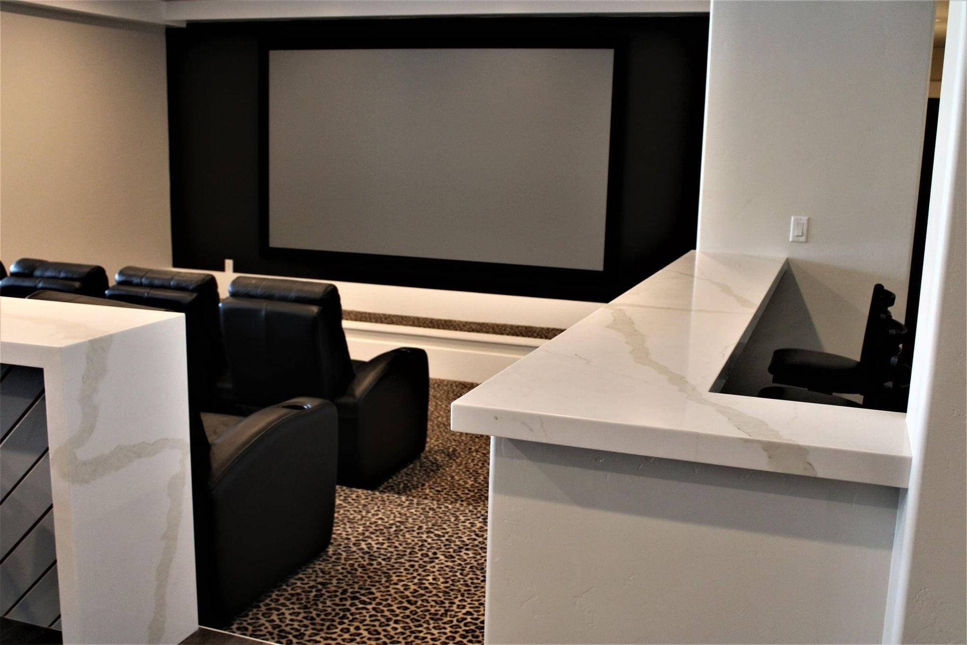 A home theater with a projector screen , chairs , and a bar.