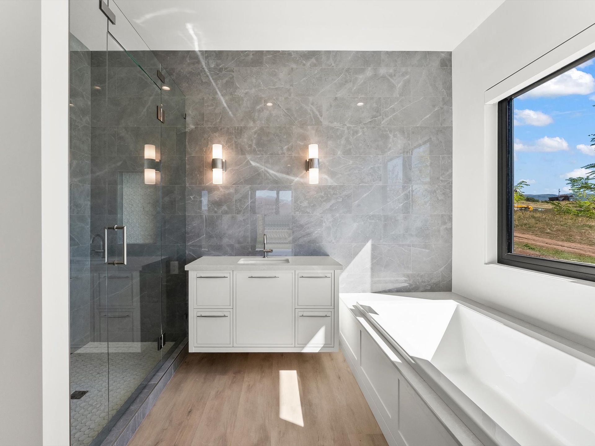 A bathroom with a tub , sink , shower and window.
