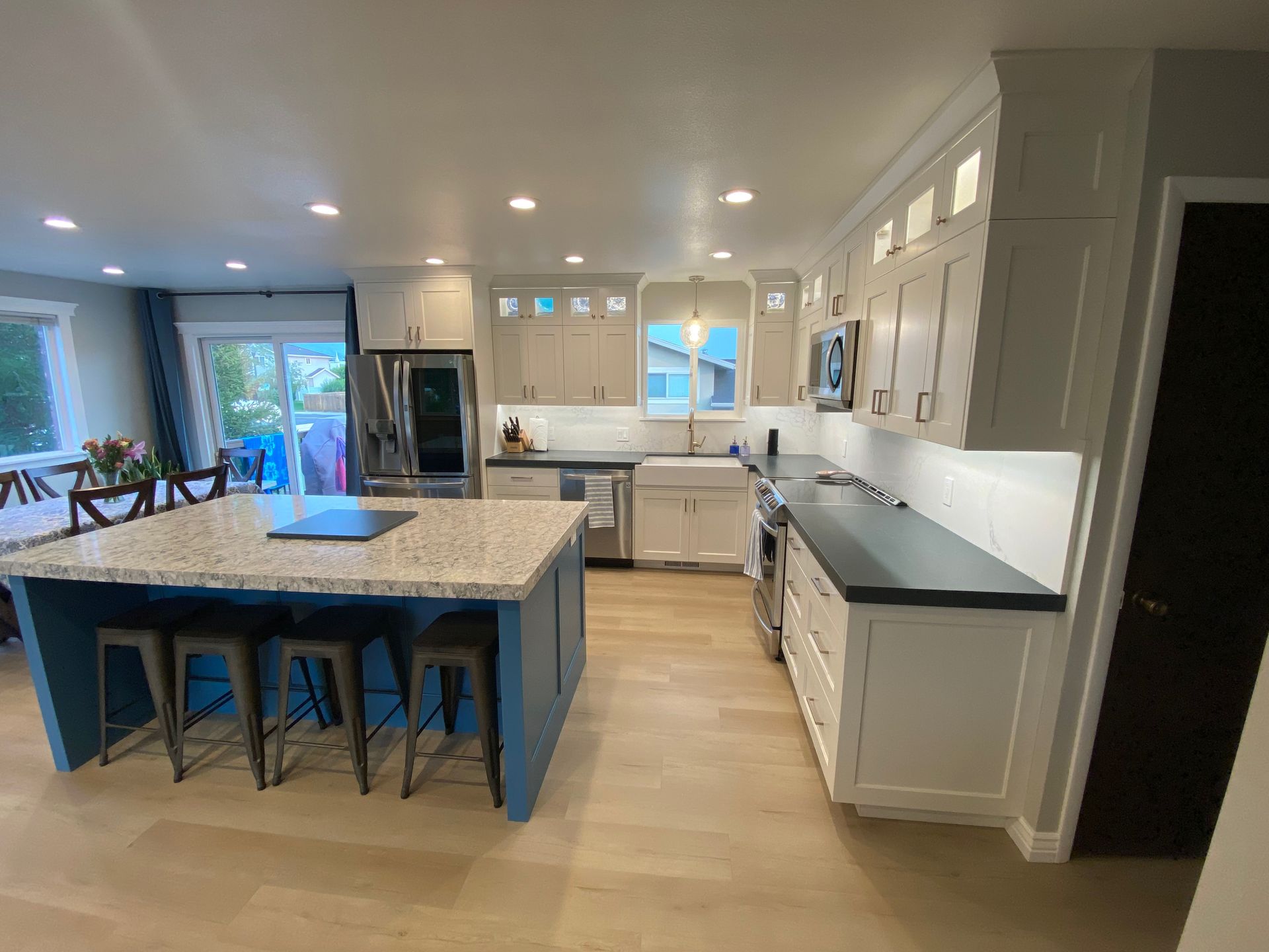 A kitchen with white cabinets , granite counter tops , stainless steel appliances and a blue island.