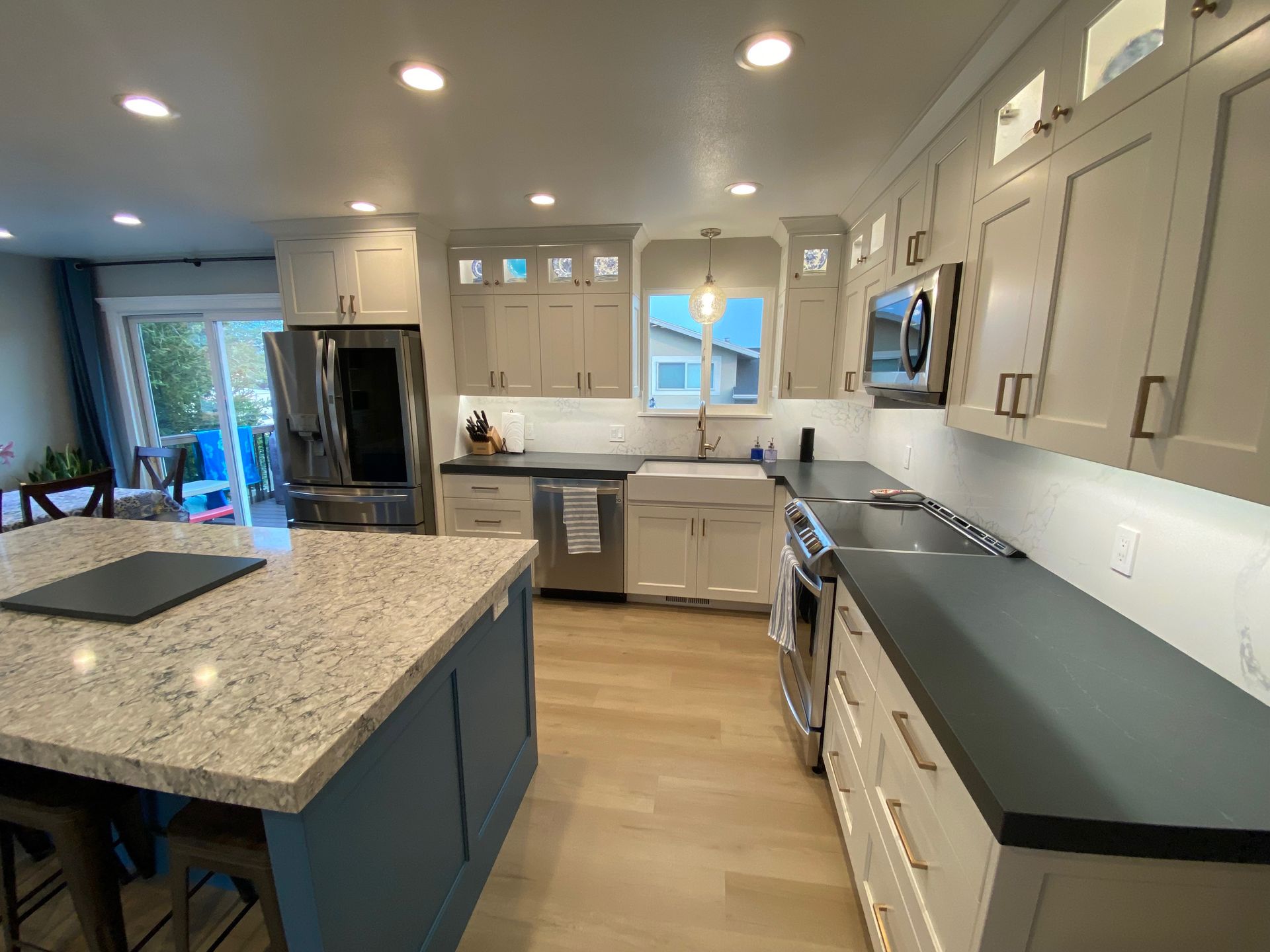 A kitchen with white cabinets , black counter tops , stainless steel appliances and a large island.