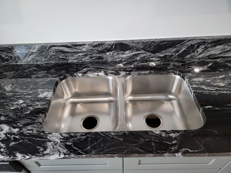 A stainless steel kitchen sink is sitting on top of a black granite counter top.