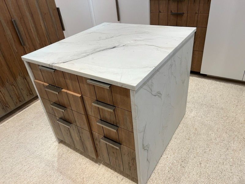 A kitchen island with a marble counter top and wooden drawers.