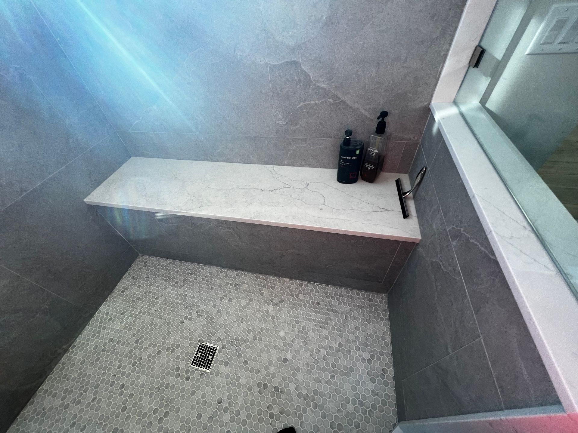 A walk in shower with a bench and a window