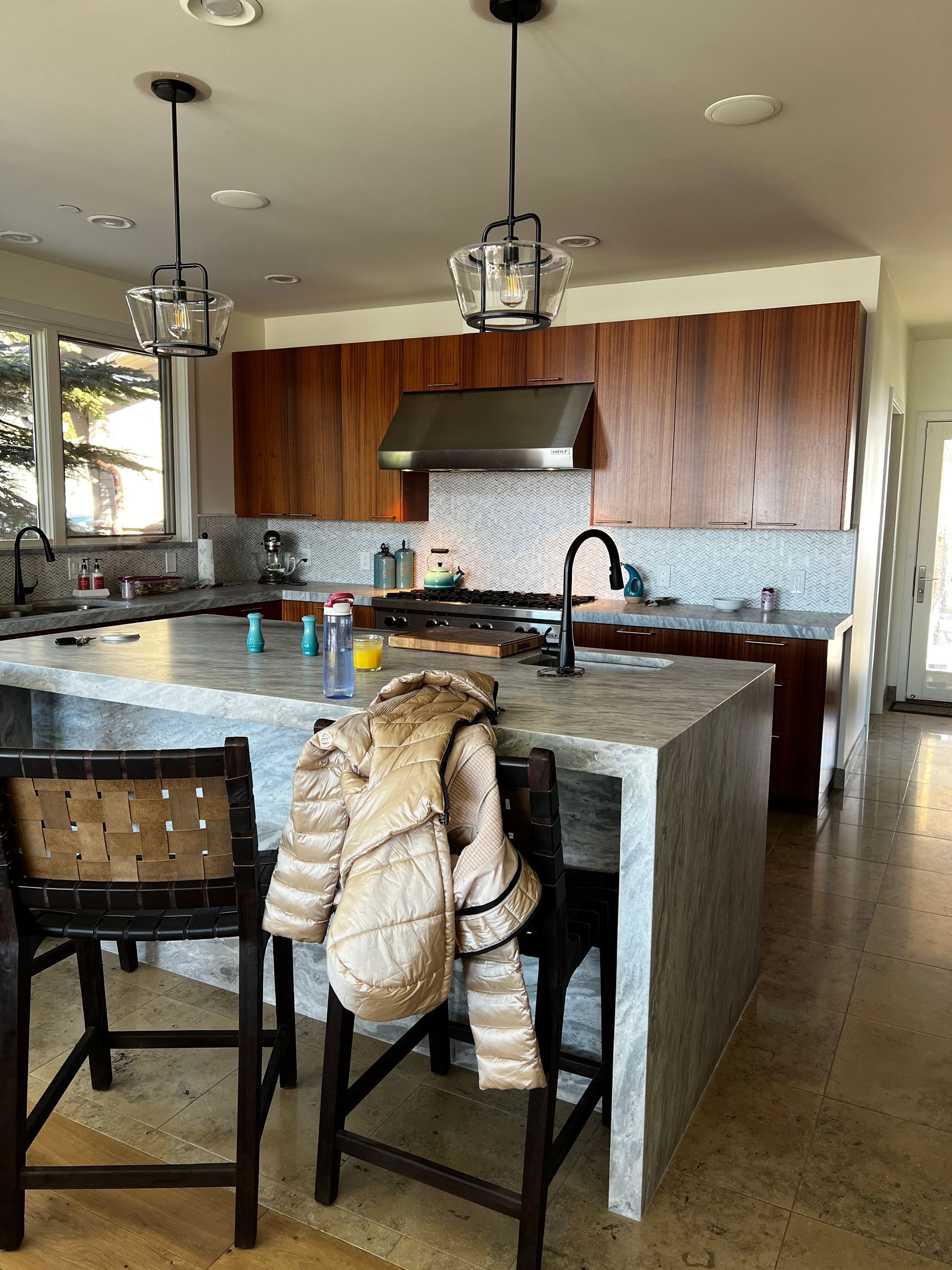 A kitchen with a large island , stools , a stove , and a jacket hanging on the counter.