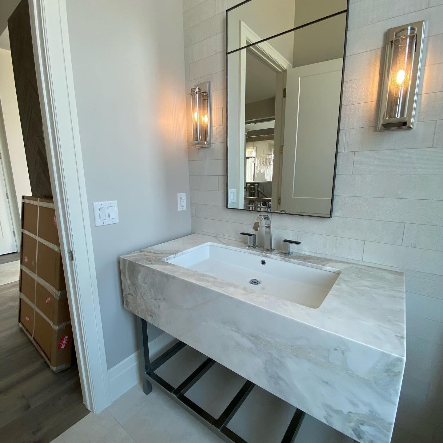 A modern bathroom with a marble sink, a large mirror, and wall-mounted sconces.
