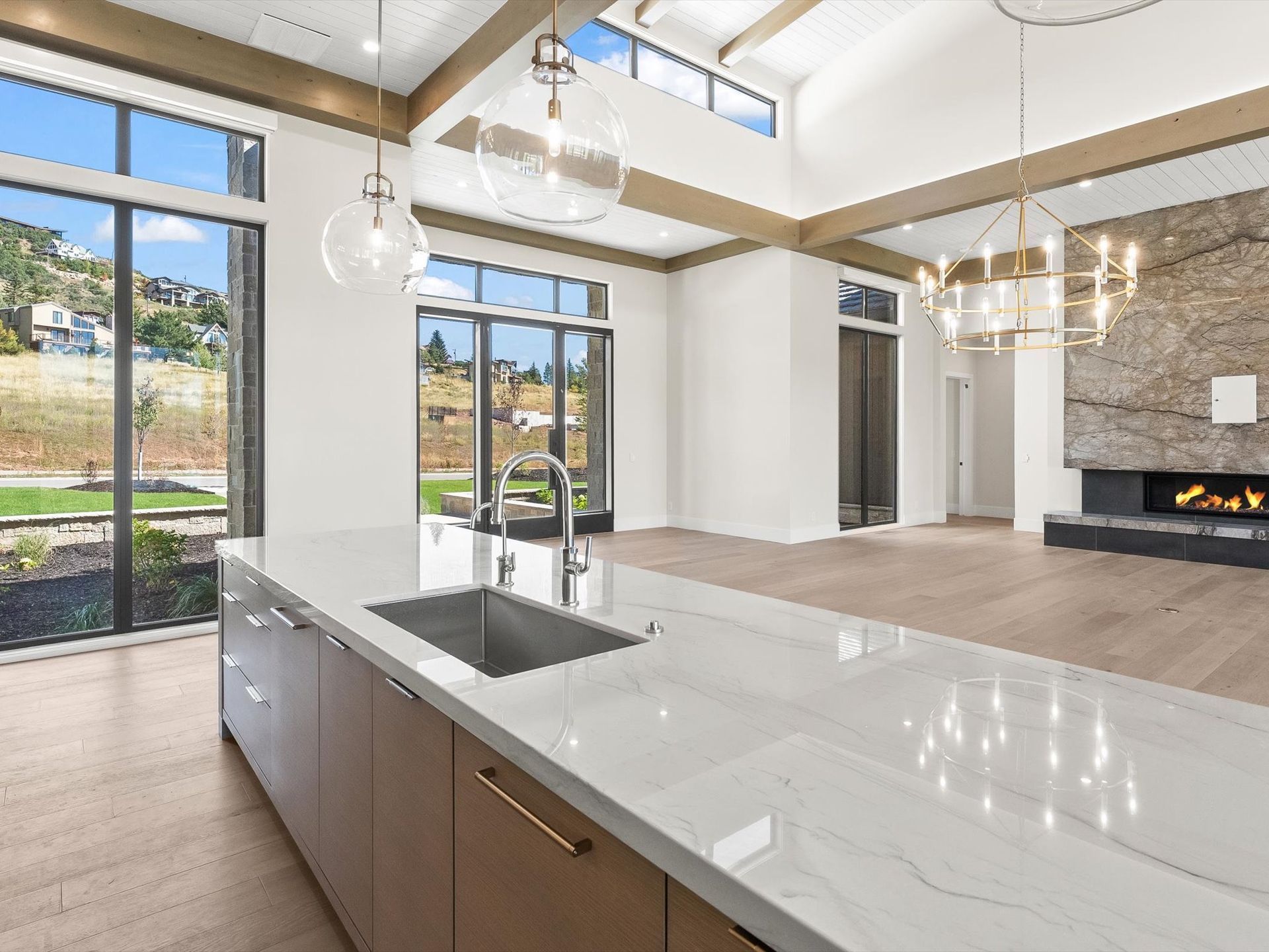 Modern kitchen with large island, windows, and a fireplace in the background