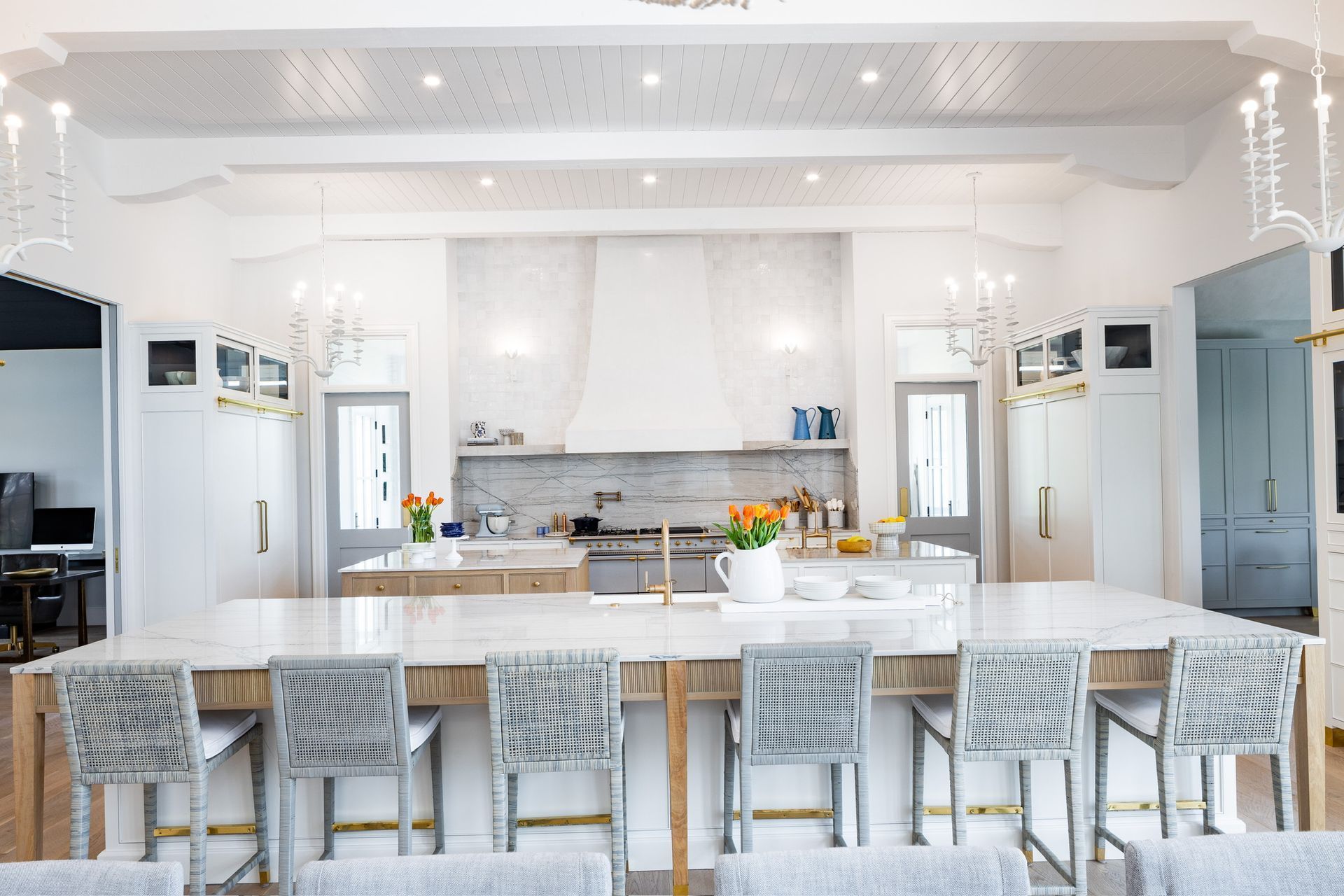 Spacious, bright white kitchen with large island, marble countertops, and decorative chandeliers.