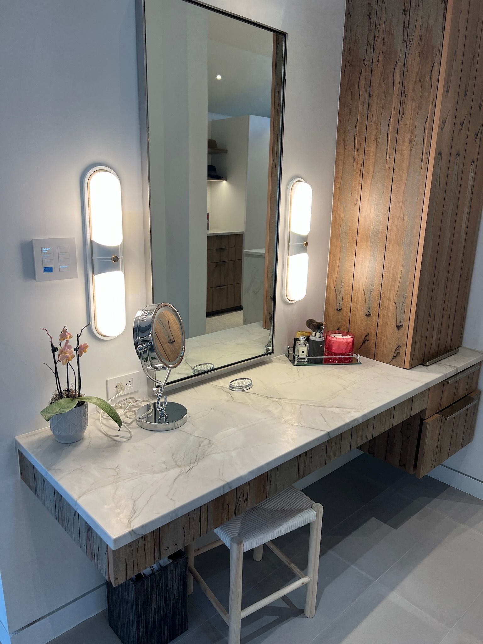 Vanity with marble top, large mirror, side lights, and decorative wooden elements