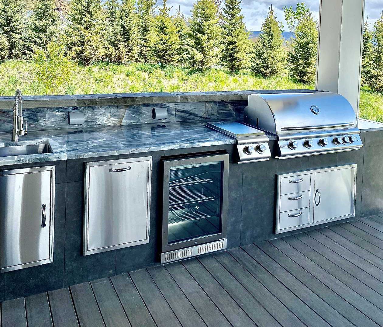 An outdoor kitchen with a grill , sink and refrigerator