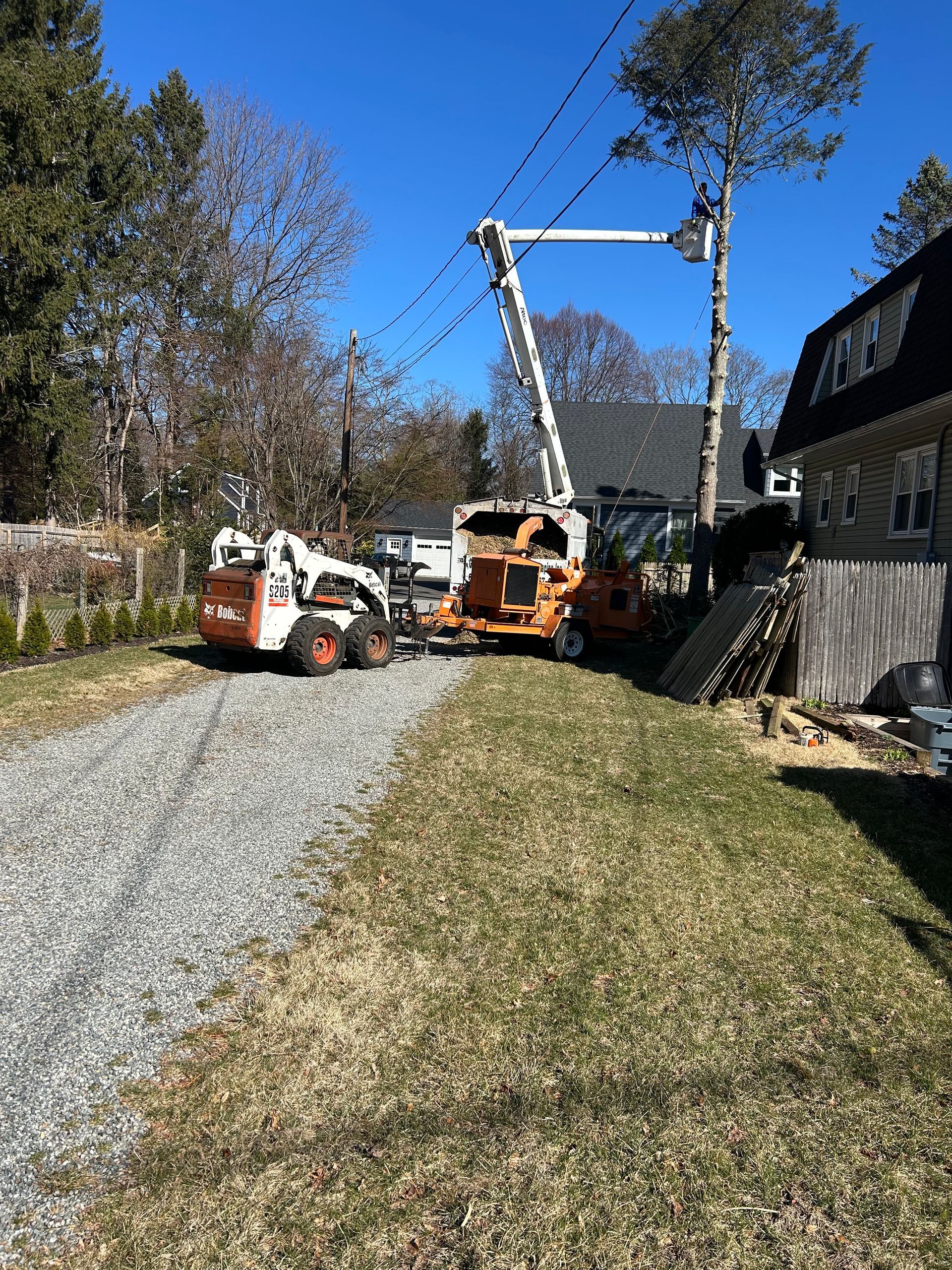 A tractor is cutting a tree in a driveway next to a house.