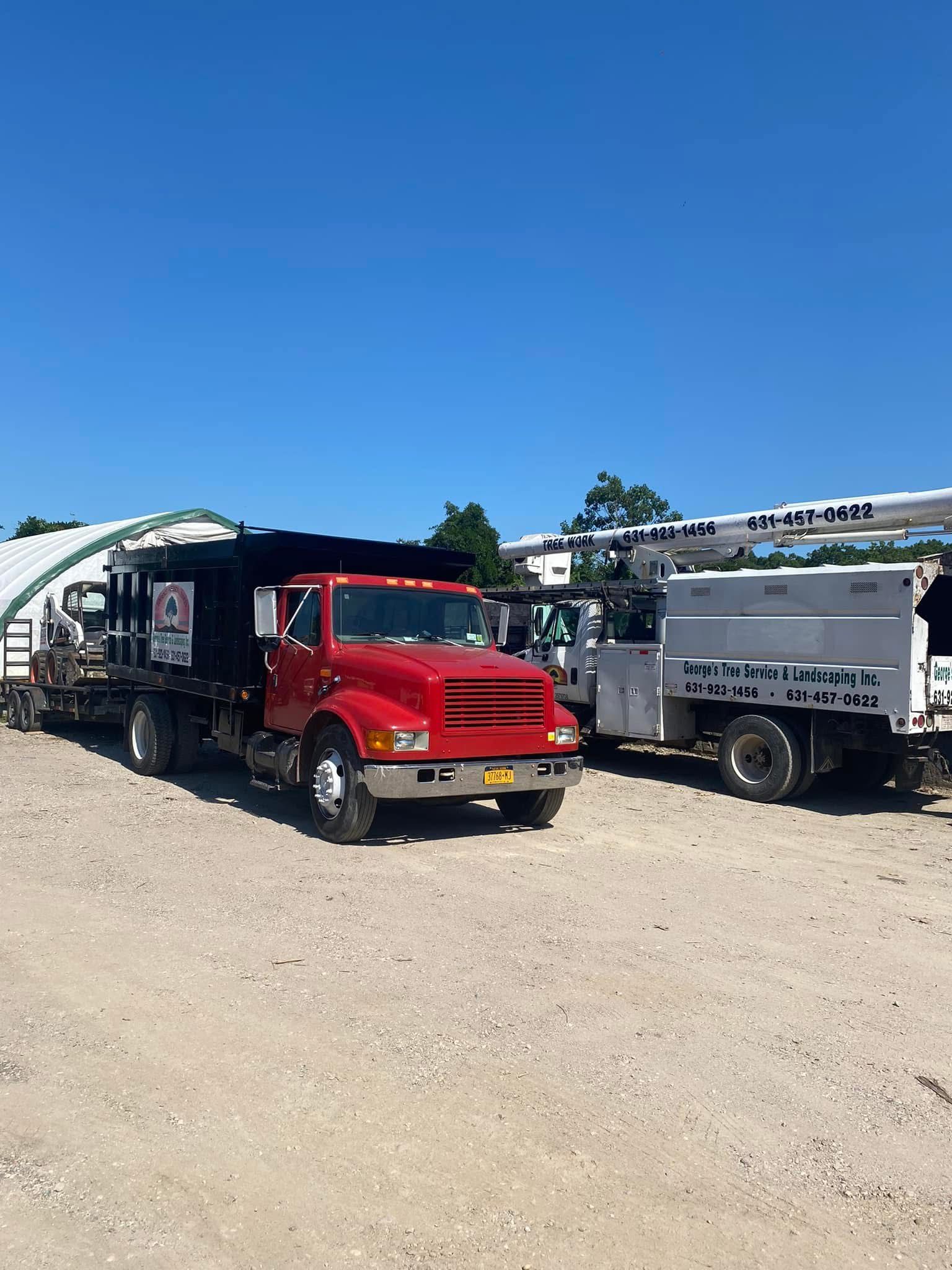 A red truck is parked next to a white truck in a dirt lot.