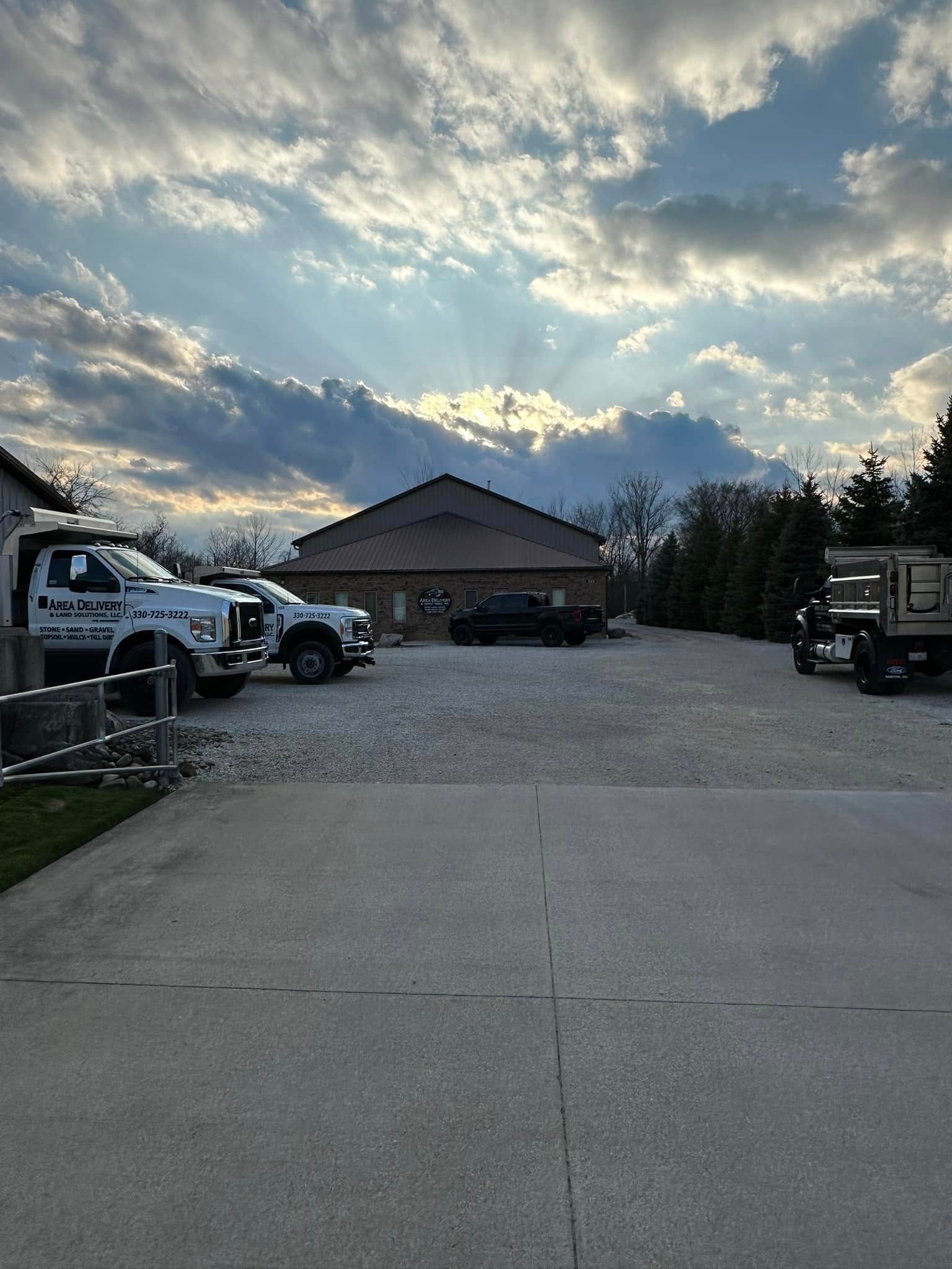 Wide driveway with trucks on both sides leading to a house under a cloudy sunset sky