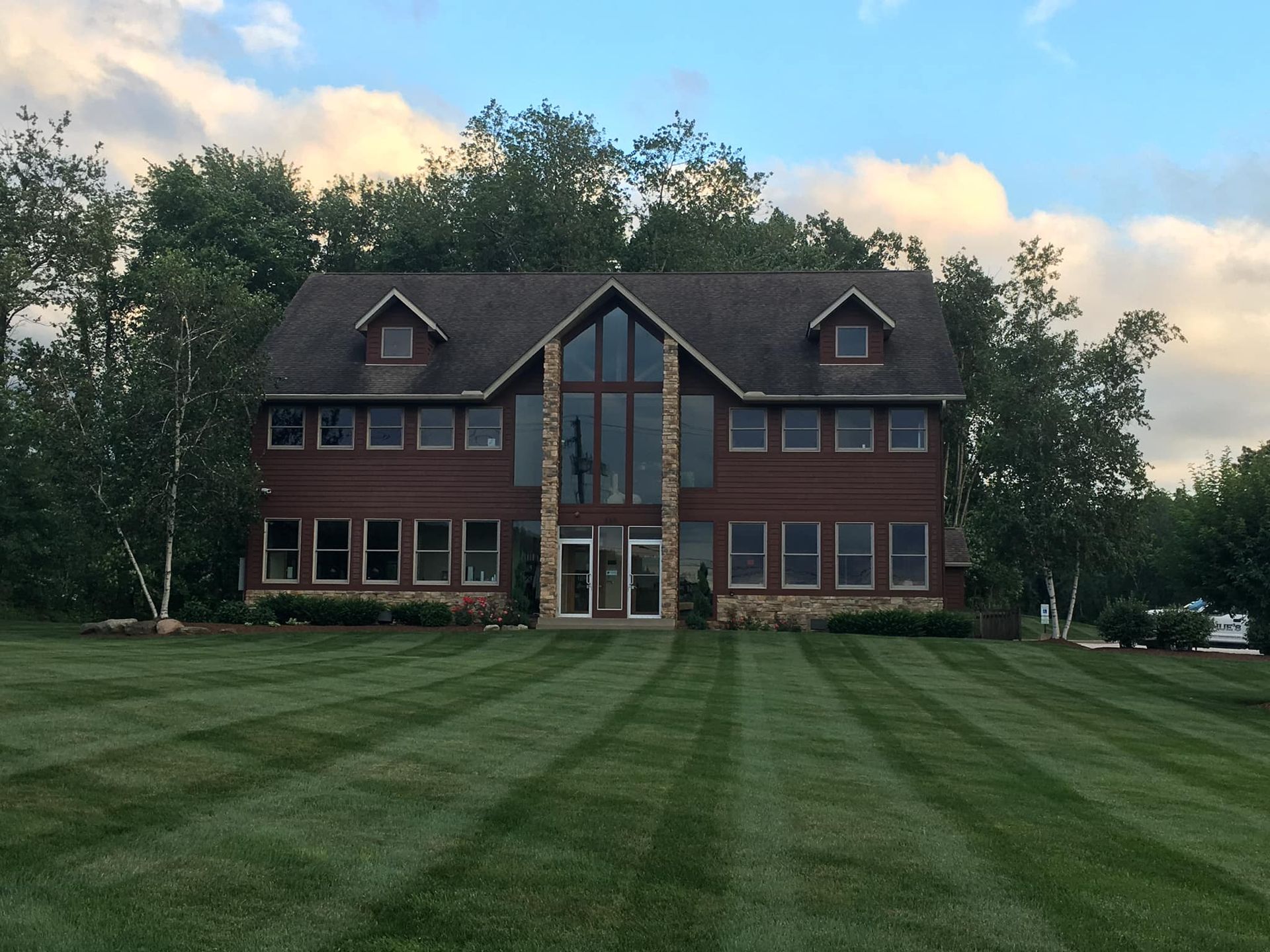 Large brick house with a steep roof and tall windows, set behind a wide green lawn at dusk
