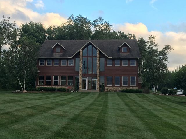 Large brick house with a steep roof and tall windows, set behind a wide green lawn at dusk
