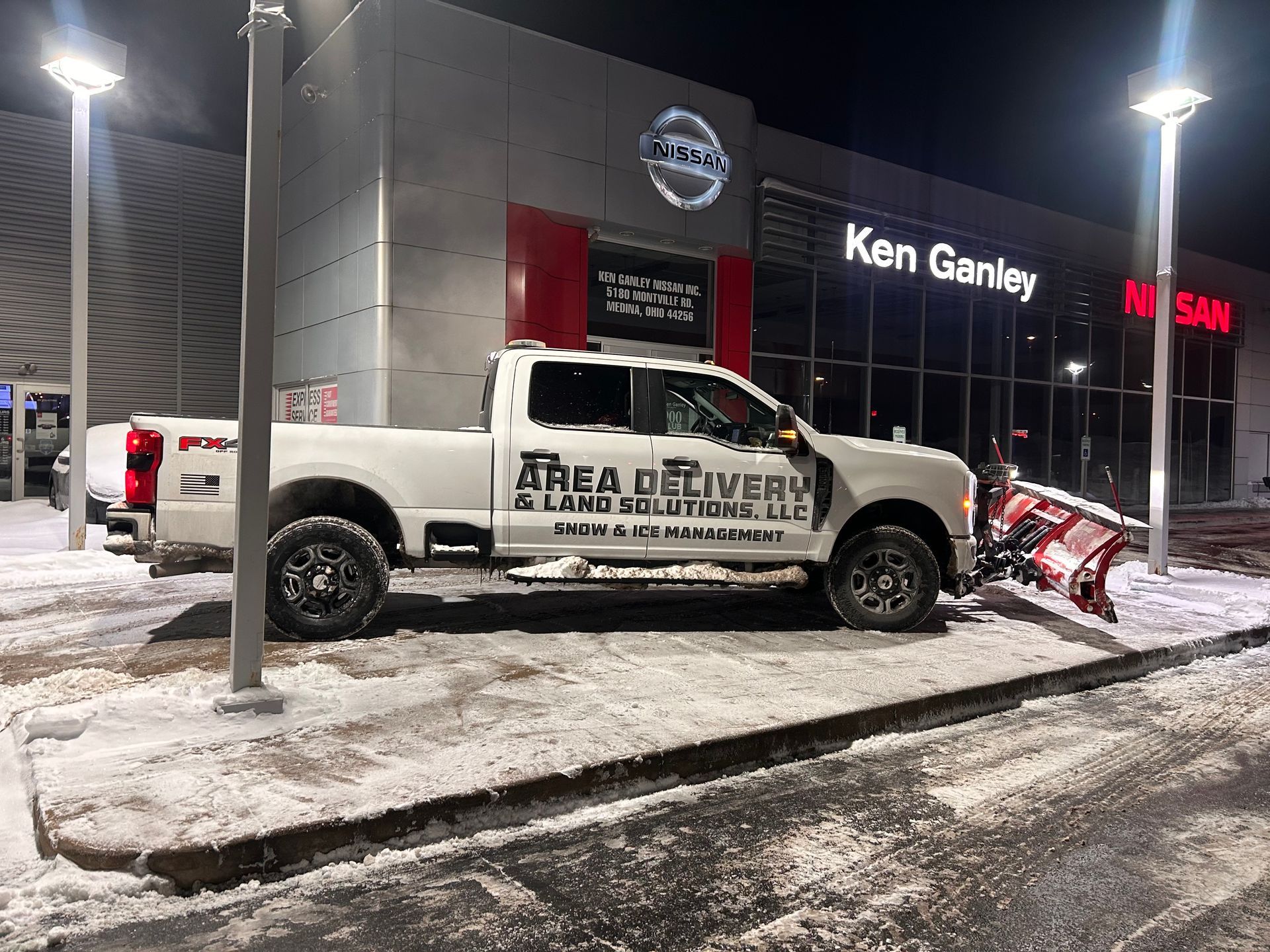 White pickup truck parked outside Ken Ganley dealership at night, with snow on the ground and a tow truck nearby