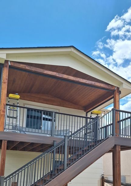 Deck with stairs and awning against a blue sky. Wooden structure, dark railing.