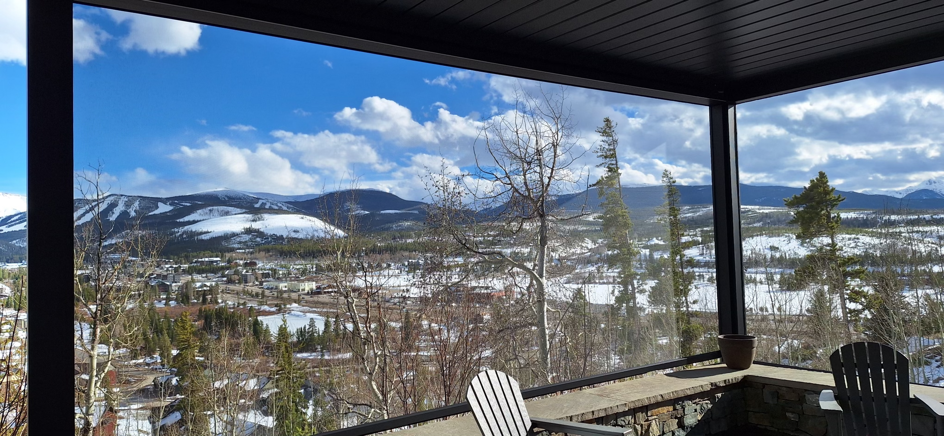 View of a snowy mountain range and town from a covered patio on a sunny day.
