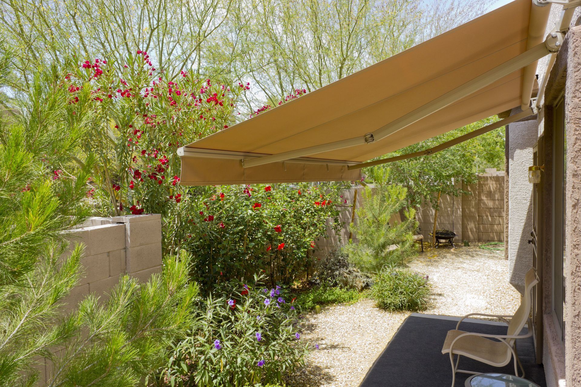 Beige awning extended over patio with chairs, surrounded by plants and a desert landscape.