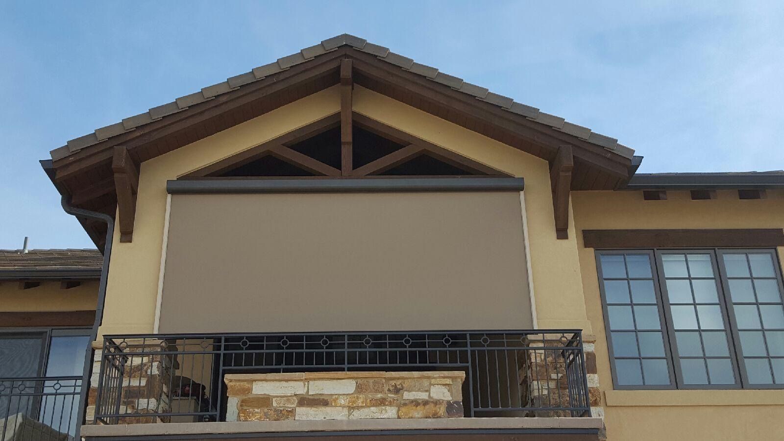 Beige awning extends over a balcony, brown roof trim, blue sky.