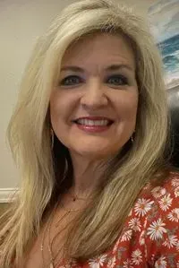 Woman with long blonde hair, smiling, wearing a floral orange top.