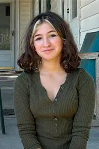 Woman with brown hair and blonde highlights, wearing a green long-sleeved shirt, smiles.