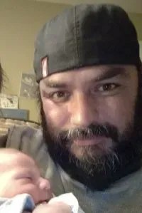 Man in black cap holds a baby close, both looking at the camera.