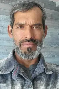 Man with graying hair and beard wearing a plaid shirt, looking directly at the camera.