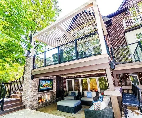 Outdoor deck with pergola, glass railings, fireplace, and lounge seating, nestled amongst trees.