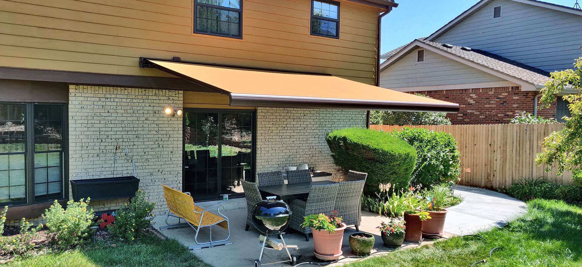 Backyard patio with awning, brick wall, patio furniture, and garden.
