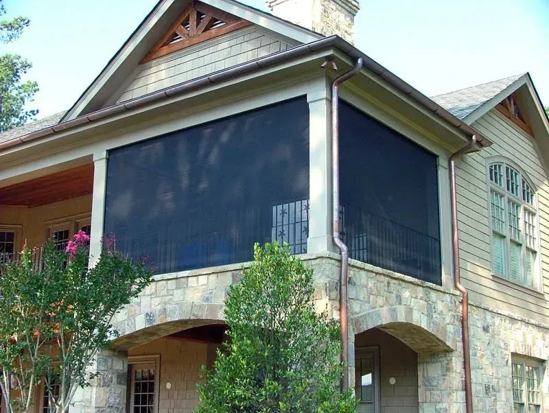 House with a screened porch, stone exterior, and dark screen shades.