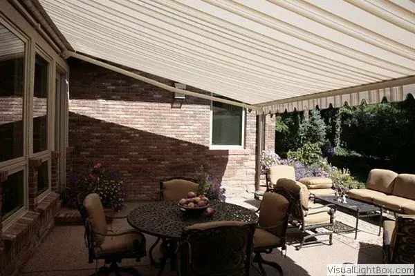 Patio with tan awning, brick wall, round table, chairs, and outdoor seating.