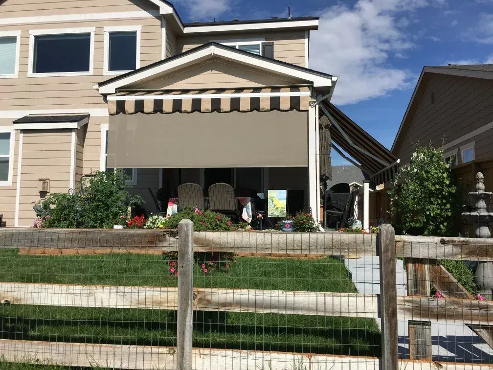 Backyard patio with beige retractable awning, grass, wooden fence, house in background.