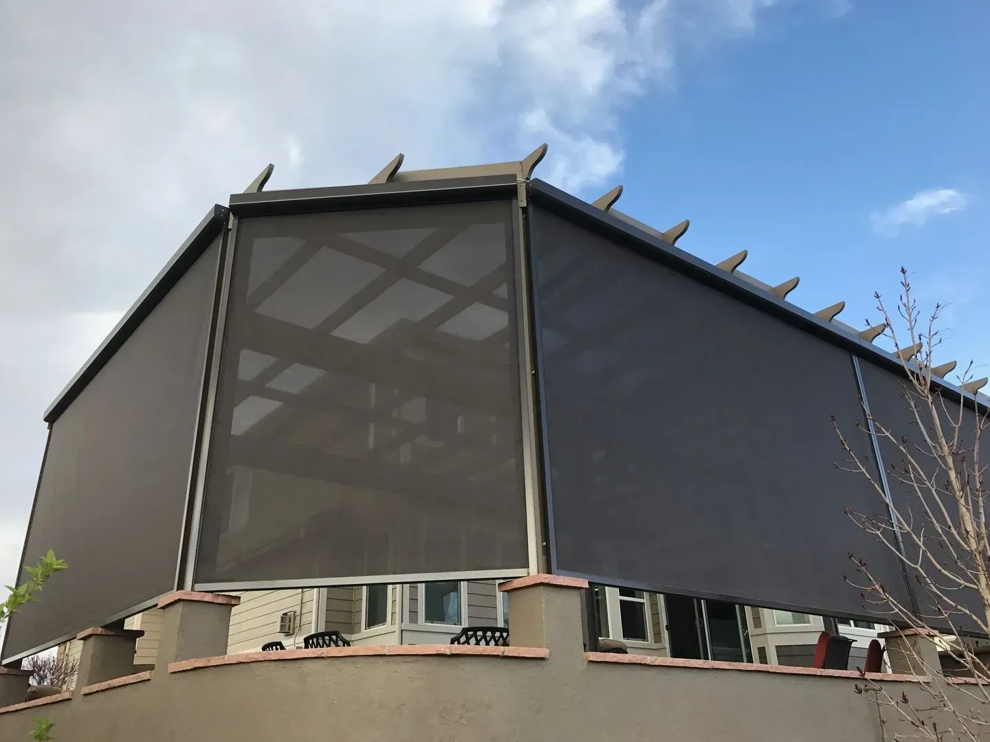 Dark brown sun shades installed on a building with a pergola, under a blue sky.