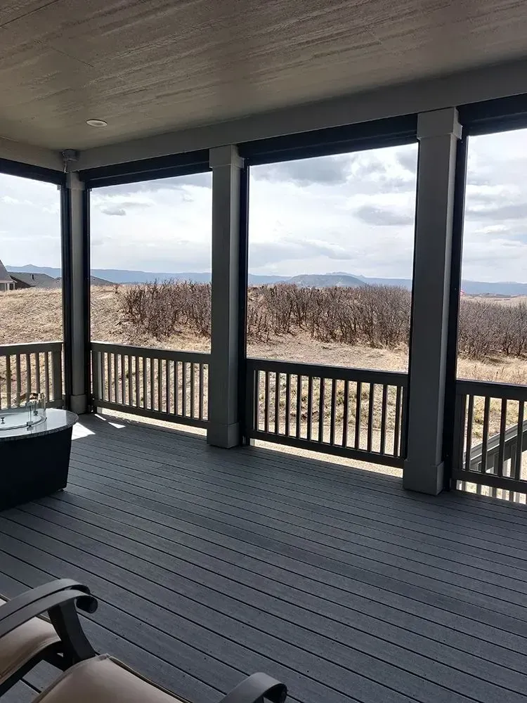Deck with gray flooring, black railing, and outdoor view through rectangular openings.