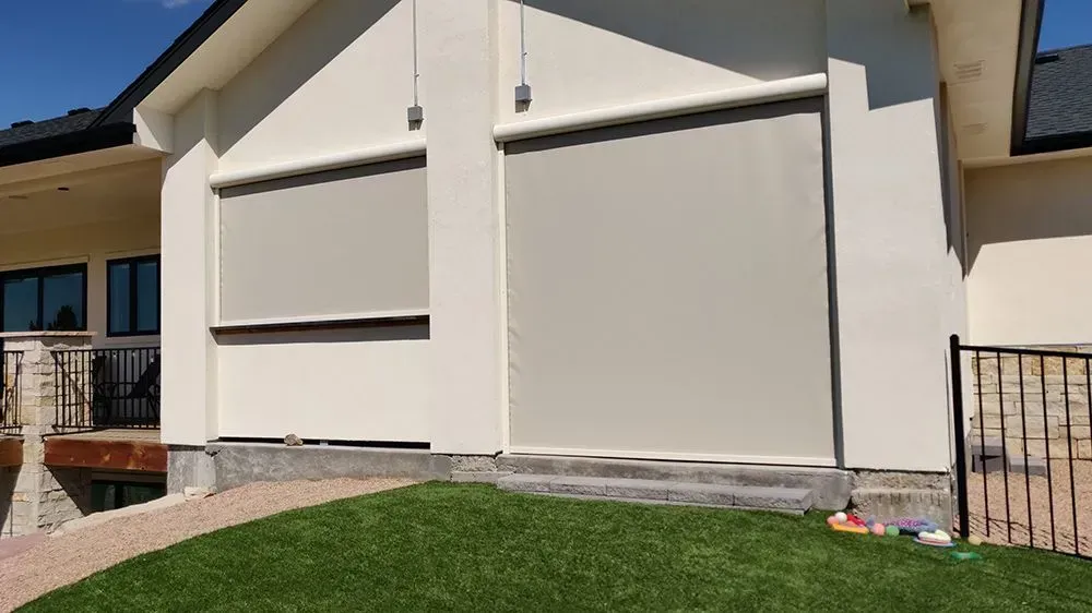 Exterior of building with two tan sun shades rolled down over windows.