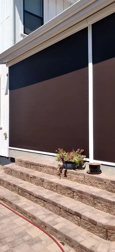 Brown and black sun shades on a house, with steps leading down to a patio area and a potted plant.