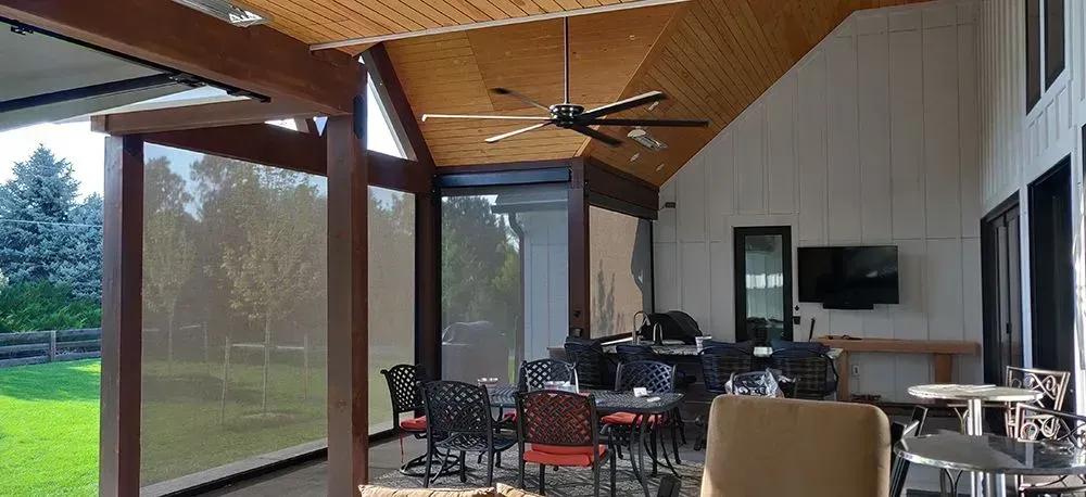 Covered outdoor patio with a dining area, ceiling fan, and television on the wall.