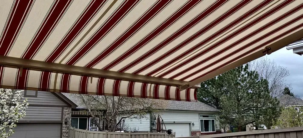 Beige and burgundy striped awning over a house with trees and a cloudy sky.